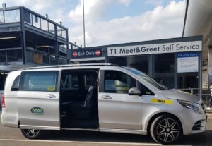 Lux Airport Transfers Ltd silver taxi van parked at T1 Meet & Greet Self Service area, ready for hire from Manchester to Stansted Airport